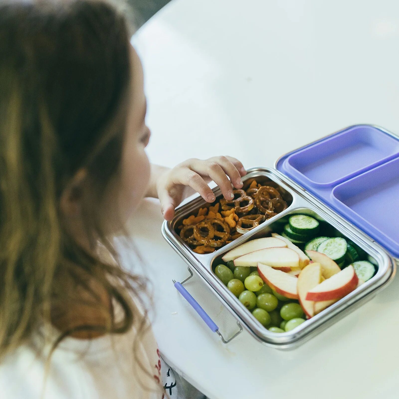 A child choosing food from a Bare Ware five-compartment stainless steel lunchbox.
