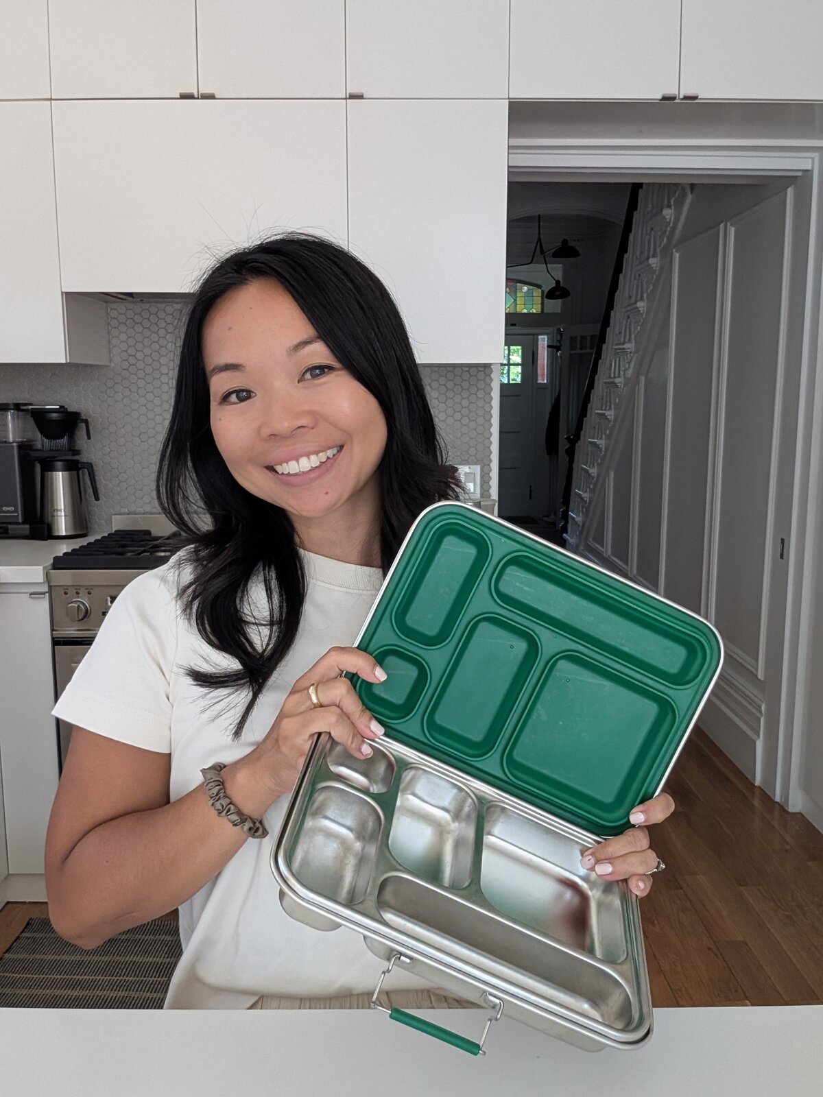 Bare Ware founder Leslie Chan holding an open stainless steel lunch box in her kitchen.
